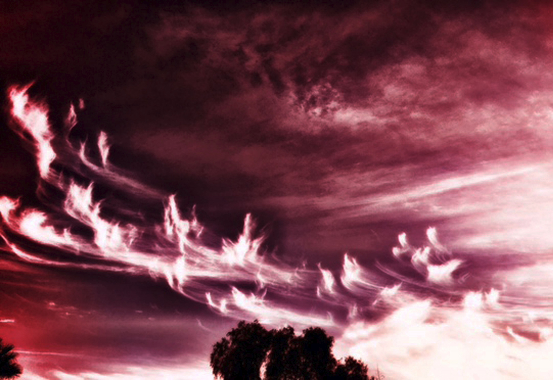 Feathered crimson cirrus clouds over a darkened horizon